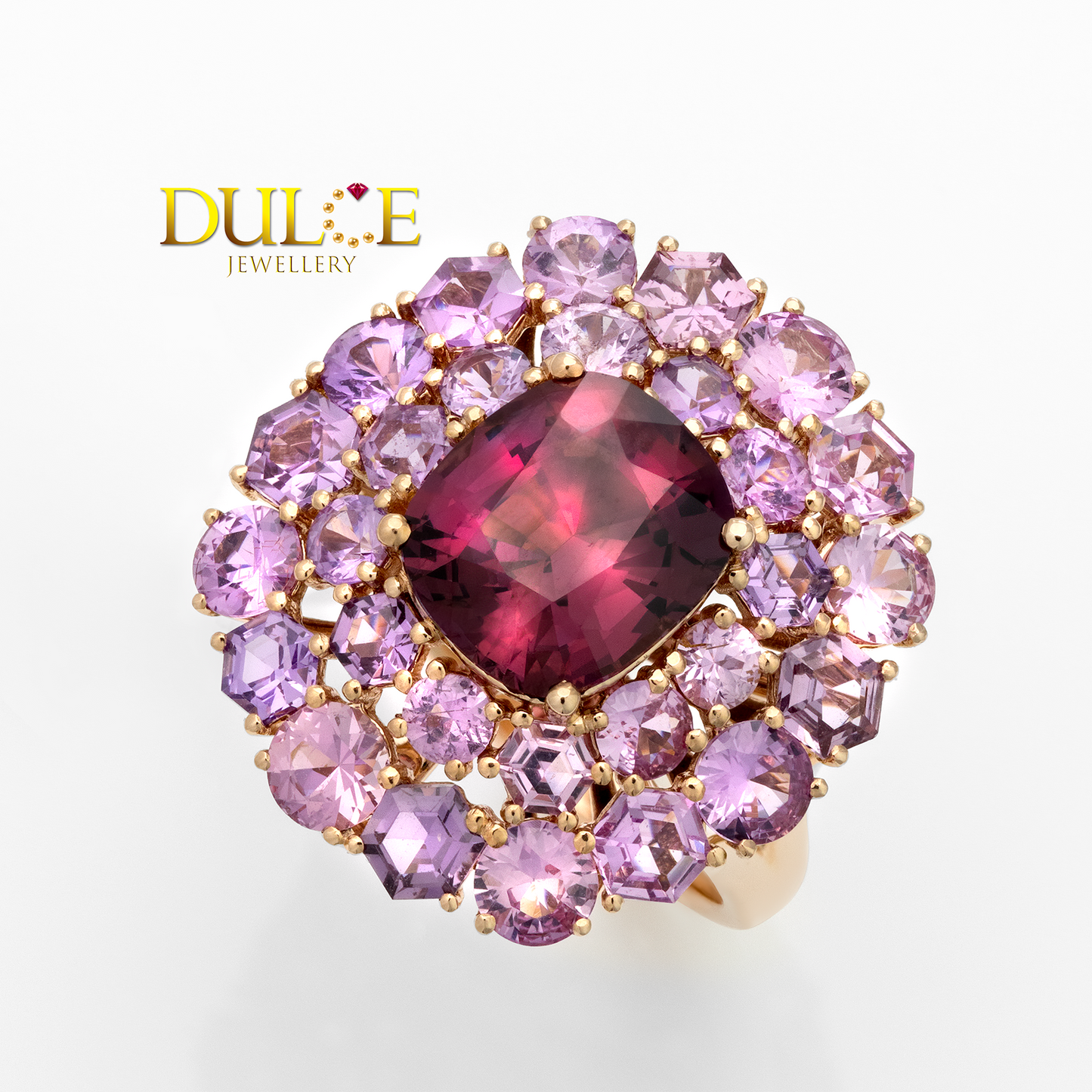 Ring with a central red gemstone surrounded by pink and purple stones on a white background, featuring the Dulce Jewellery logo.