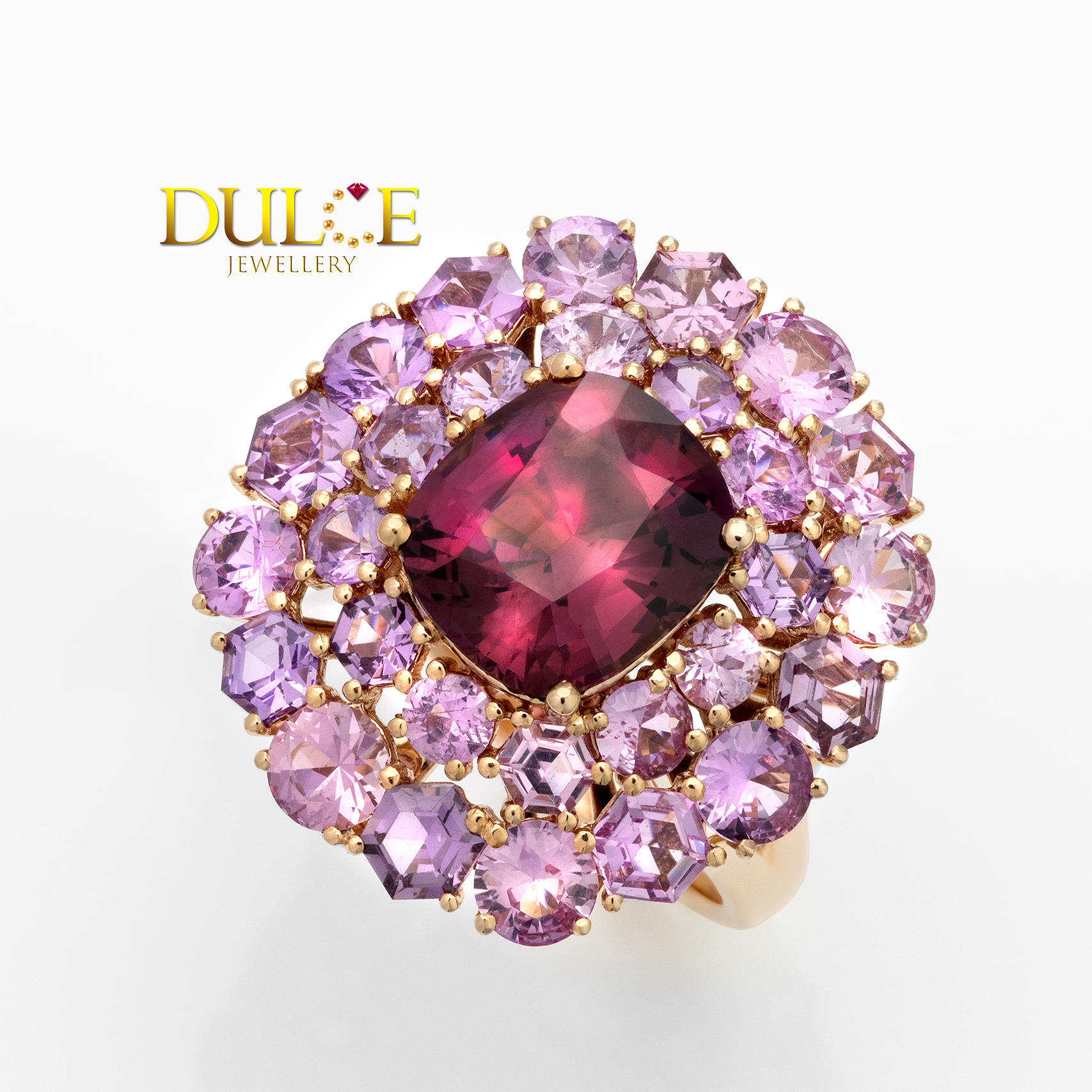 Ring with a central red gemstone surrounded by pink and purple stones on a white background, featuring the Dulce Jewellery logo.
